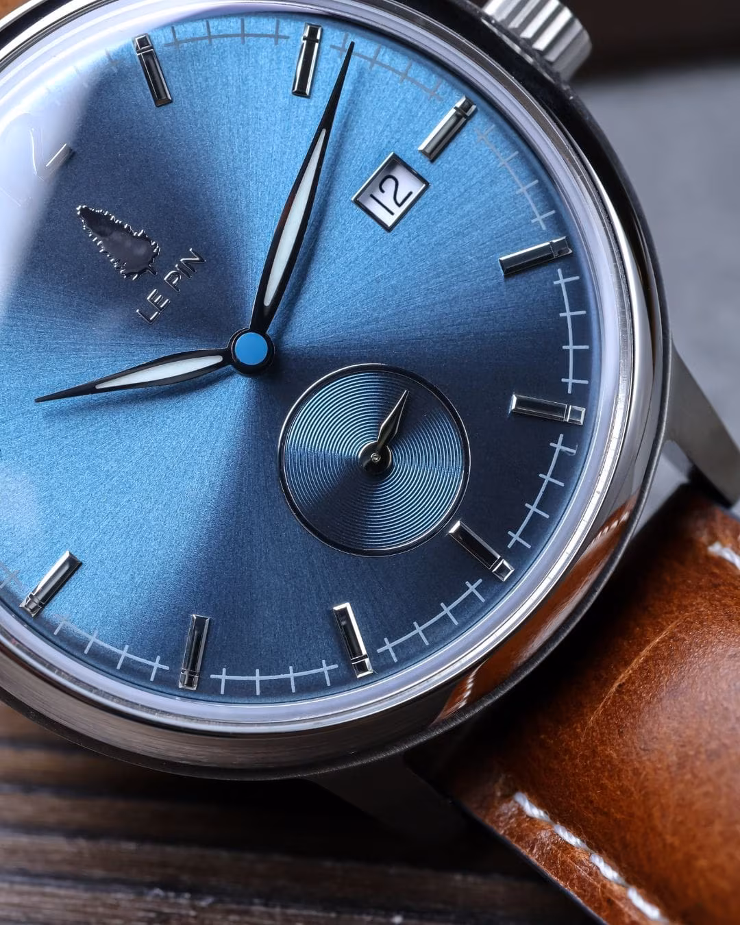 Macro view of the Le Pin blue sunburst dial, showing the applied indices, date window and small seconds sub-dial.