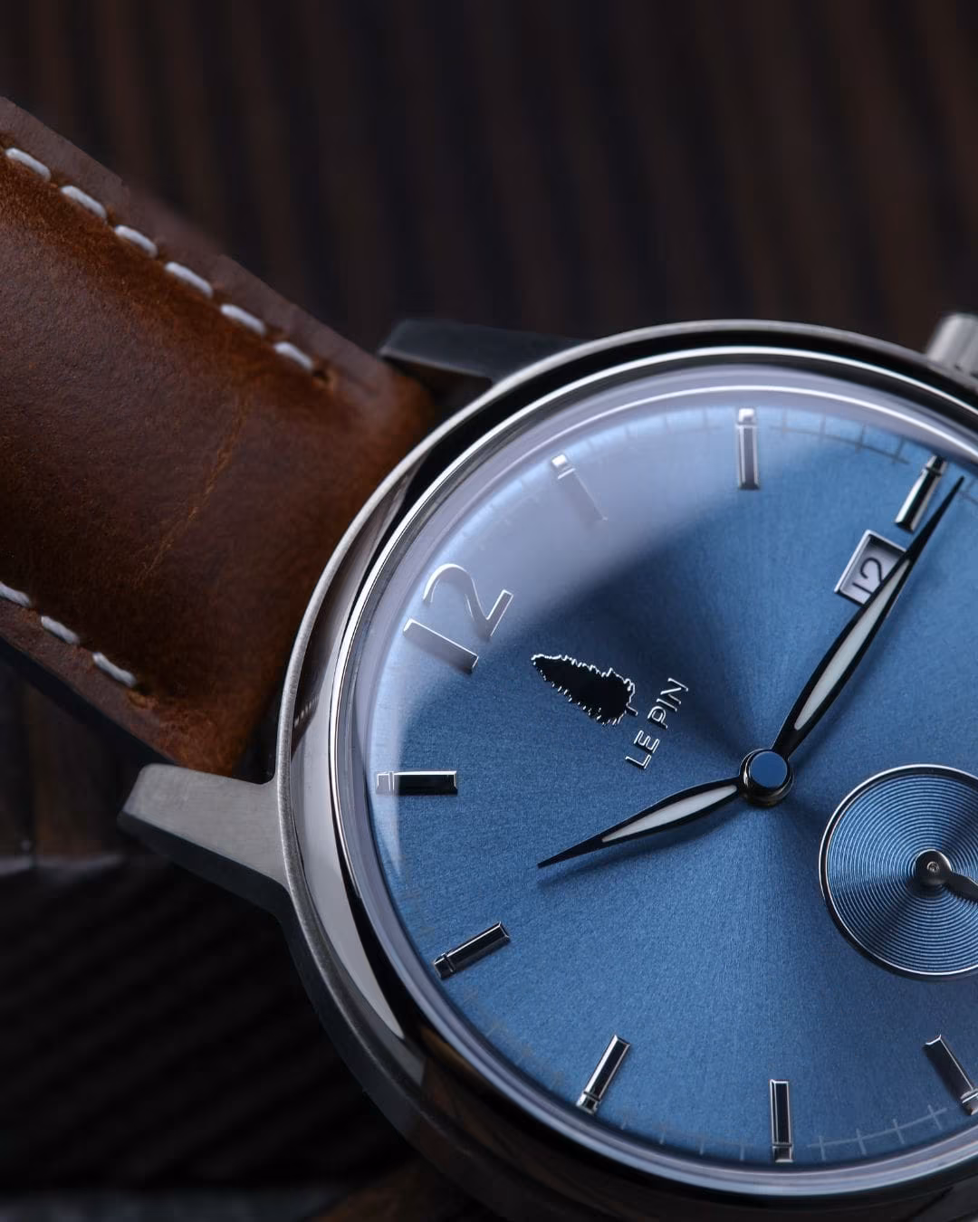 Le Pin dial with the engraved pine-tree emblem and wordmark, on a brown leather strap.