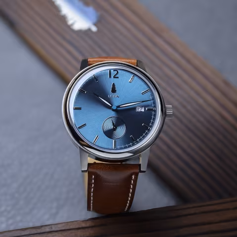 The Le Pin watch standing upright on ribbed wood beside a single pine needle.